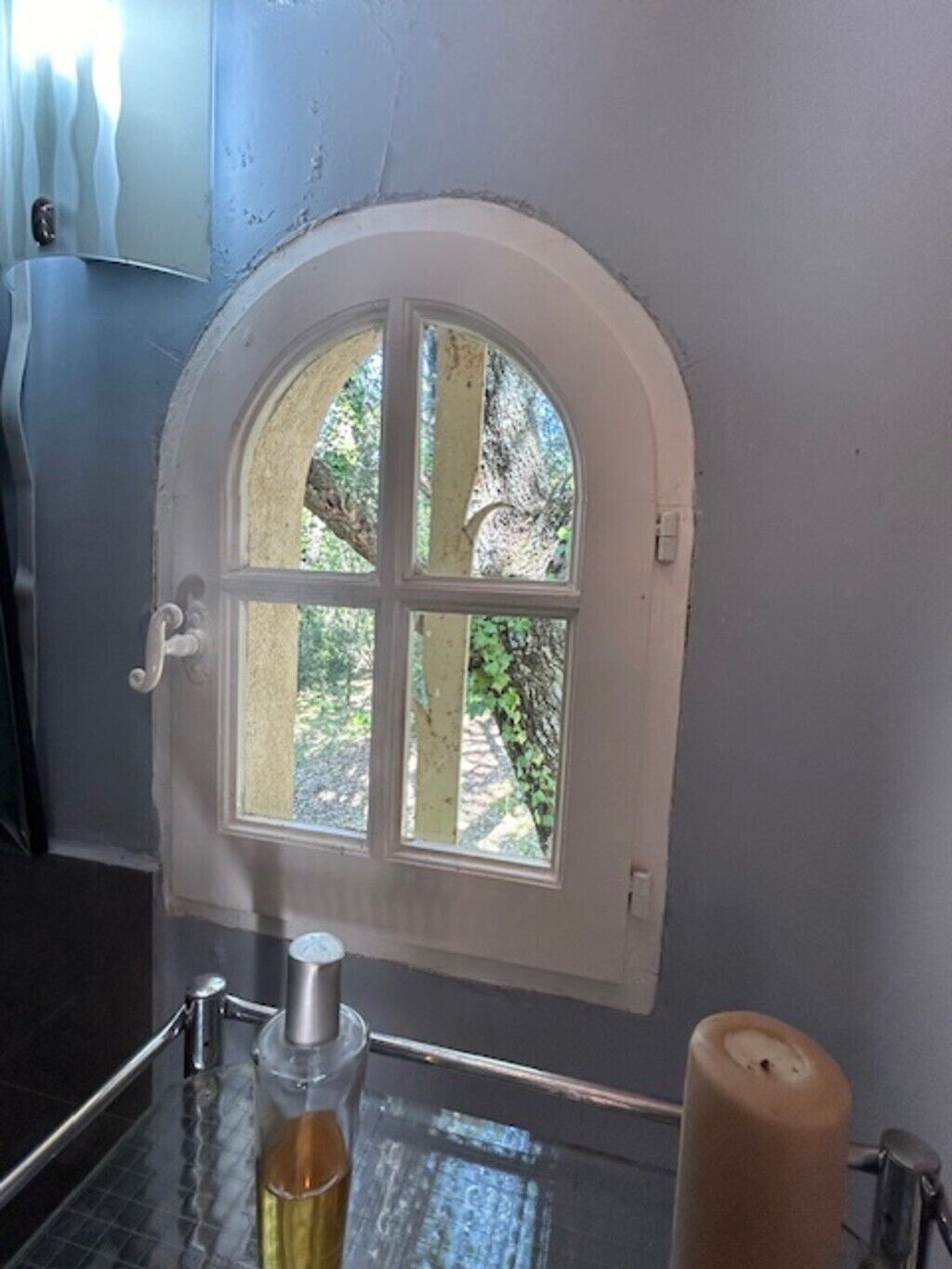 A bathroom with a small arched window, a glass bottle, and a candle on the counter.
