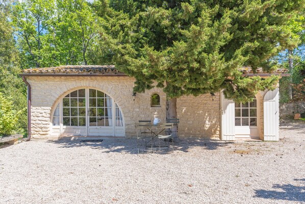 A stone building with a tiled roof, a large arched window, and a door.