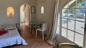 A room with a bed, a table with chairs, a window with curtains, and a view of the outside. - Holiday Home 'Orangerie' with Mountain View, Shared Terrace and Wi-Fi (Bonnieux)