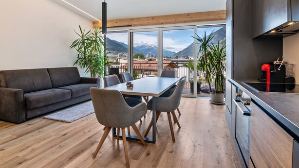 A modern living room with a sofa, dining table, chairs, and a kitchen area. - Apartment 'Penthouse -  Venosta' with Mountain View, Balcony and Wi-Fi (Naturno)