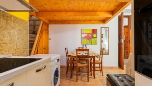 A compact kitchen with a washing machine, a dining table with chairs, and a wooden ceiling. - Apartment 'Casa Musio' (Cagliari)
