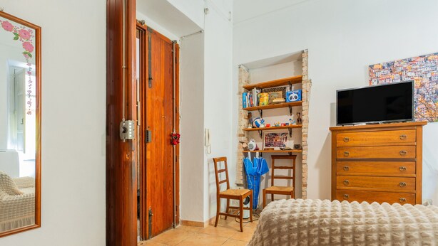 A bedroom with a wooden wardrobe, a television, a bookshelf, and a bed with a patterned blanket. - Apartment 'Casa Musio' (Cagliari)