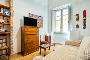 A room with a wooden dresser, a television, a window with curtains, and a wall with masks. - Apartment 'Casa Musio' (Cagliari)