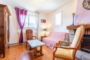 A room with a bed, a table, a chair, a fireplace, and a clock on the wall. - Holiday Home 'Nicole Face Mer' with Sea View, Private Terrace and Wi-Fi (Trégunc)