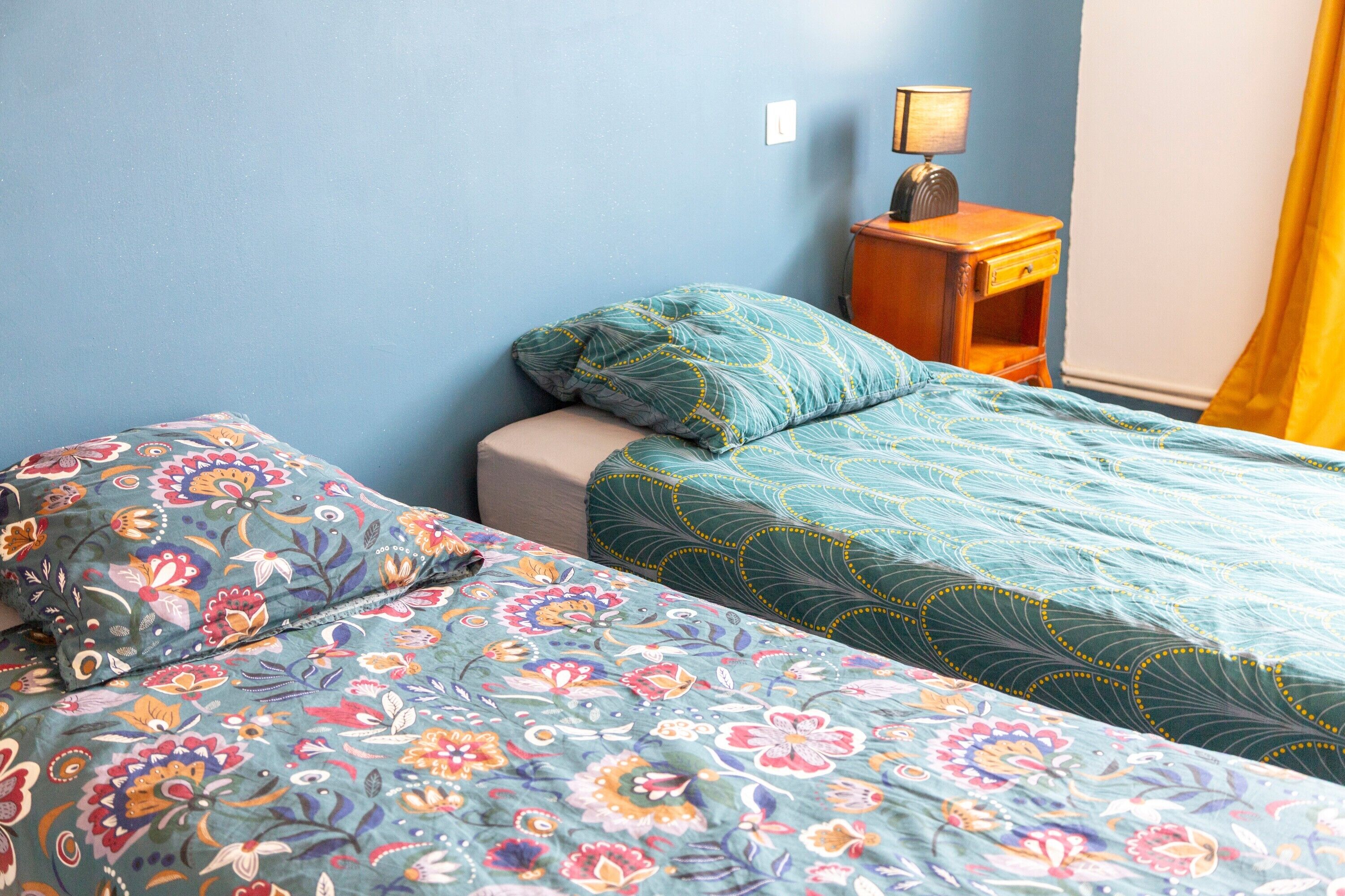 A bedroom with two beds, a nightstand, a lamp, and a window with curtains.