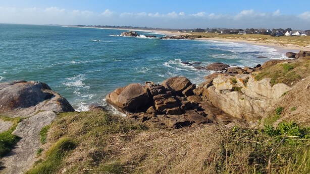Een kustlandschap met rotsformaties, een strand en huizen in de verte.
