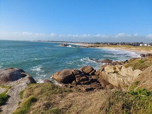 A coastal landscape with rocky outcrops, a beach, and houses in the distance. - Holiday Home 'Nicole Face Mer' with Sea View, Private Terrace and Wi-Fi (Trégunc)