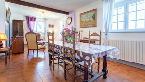 Een eetkamer met een houten tafel en stoelen, een klok aan de muur en een raam met gordijnen.
