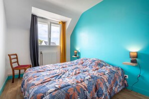A bedroom with a bed, a chair, a window, a wall-mounted lamp, and a radiator. - Holiday Home 'Nicole Face Mer' with Sea View, Private Terrace and Wi-Fi (Trégunc)