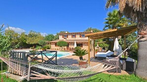 A pool area with a hammock, outdoor furniture, and a stone building in the background. - Villa 'Carbonell' with Mountain View, Wi-Fi and Air Conditioning (Alcudia)
