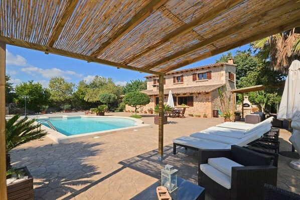 A poolside area with a stone pool, outdoor furniture, and a building with a stone facade.