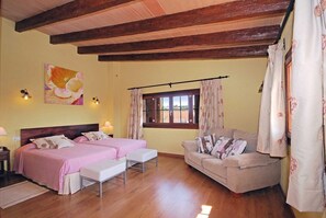 A room with two beds, a sofa, a window with curtains, and a painting on the wall.
