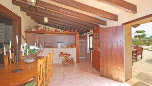 A rustic kitchen with wooden beams, a dining area with a table and chairs, and a view of the outdoors. - Villa 'Carbonell' with Mountain View, Wi-Fi and Air Conditioning (Alcudia)