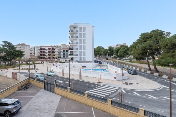 A modern building with a central courtyard, a parking area, and a street with cars and a pedestrian crossing.