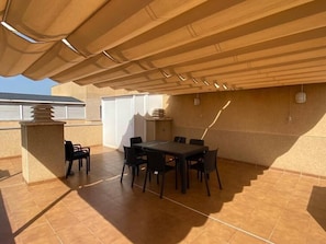 An outdoor patio with a table and chairs, a covered area, and a building in the background. - Apartment 'Mar de Laura' with Shared Pool, Private Terrace, and Shared Garden (Miami Playa)