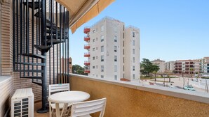 A balcony with a white table and chairs, a black metal railing, and a view of a multi-story building. - Apartment 'Mar de Laura' with Shared Pool, Private Terrace, and Shared Garden (Miami Playa)