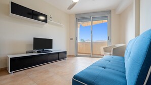 A living room with a flat-screen TV, a blue sofa, a ceiling fan, and a sliding glass door leading to an outdoor area. - Apartment 'Mar de Laura' with Shared Pool, Private Terrace, and Shared Garden (Miami Playa)
