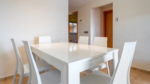 A dining area with a white table and chairs, a wooden door, and a small window. - Apartment 'Mar de Laura' with Shared Pool, Private Terrace, and Shared Garden (Miami Playa)