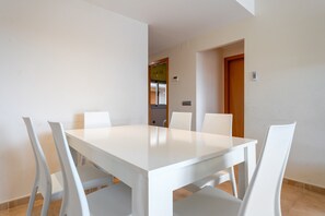 Un comedor con una mesa y sillas blancas, una puerta de madera y un ventanal pequeño.