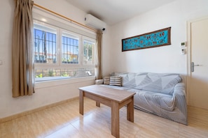 Une pièce avec une fenêtre, un canapé, une table et un climatiseur fixé au mur.