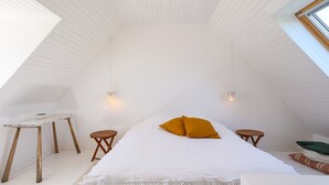 Ein Zimmer mit hohen Decken, einem Bett, zwei kleinen Tischen und einer schrägen Deckenfläche.
