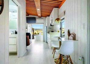 A modern kitchen with white cabinetry, a wooden ceiling, and a view of a mountainous landscape.