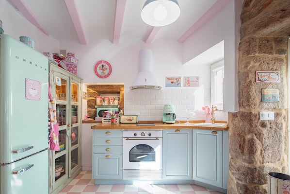 A kitchen with a vintage refrigerator, a stove, and a stone wall.