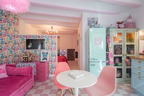 A pink-themed room with a checkered floor, a pink sofa, a white table, and a vintage-style refrigerator.