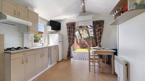 A compact kitchen with a stove, refrigerator, and a TV mounted on the wall.