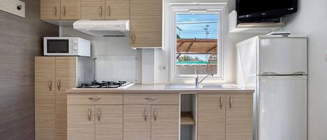 A modern kitchen with wooden cabinets, a microwave, a gas stove, a refrigerator, and a TV mounted above the sink.