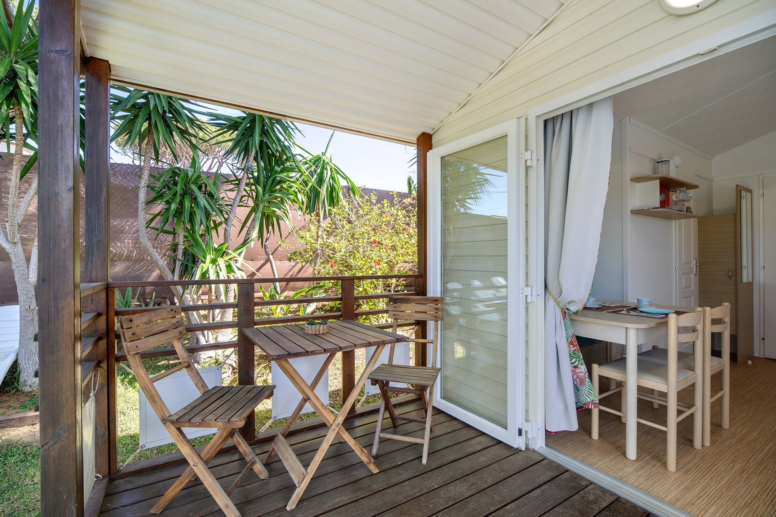 Eine Holzterrasse mit Tisch und Stühlen, einer Schiebeglastür und einer kleinen Küchenzeile.