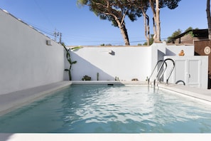Une piscine avec un mur blanc, une échelle en métal et une petite porte.
