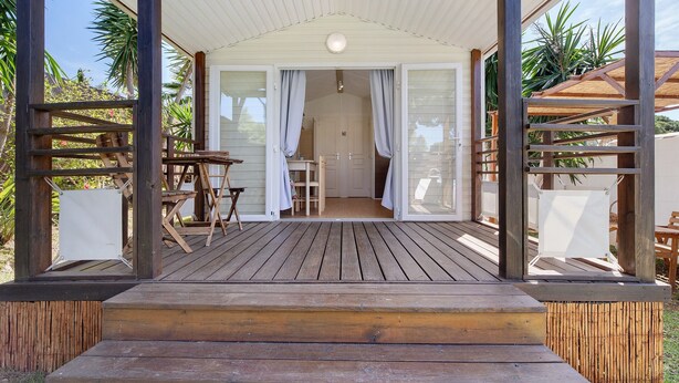 A wooden deck with a covered seating area, a small table, and a chair.