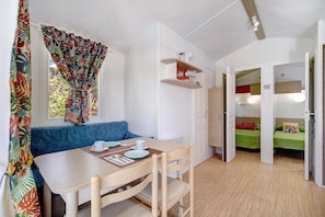 Une pièce comprenant une table à manger, des chaises, un canapé bleu, un lit avec une couverture verte et une petite étagère avec divers objets.