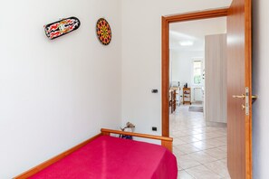 Une pièce comprenant un lit, un jeu de fléchettes et une porte donnant sur un espace cuisine.