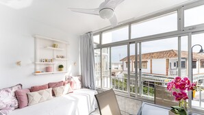 A hotel room with a bed, a chair, a table, a window with a view of buildings, and a ceiling fan. - Studio Apartment 'Butiplaya Frontline Beach' with Sea View, Wi-Fi and Air Conditioning (La cala de Mijas)