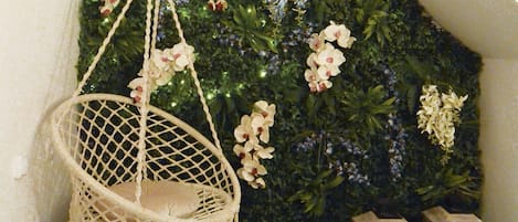 Una silla colgante, dos faroles y una pared decorada con plantas y flores.