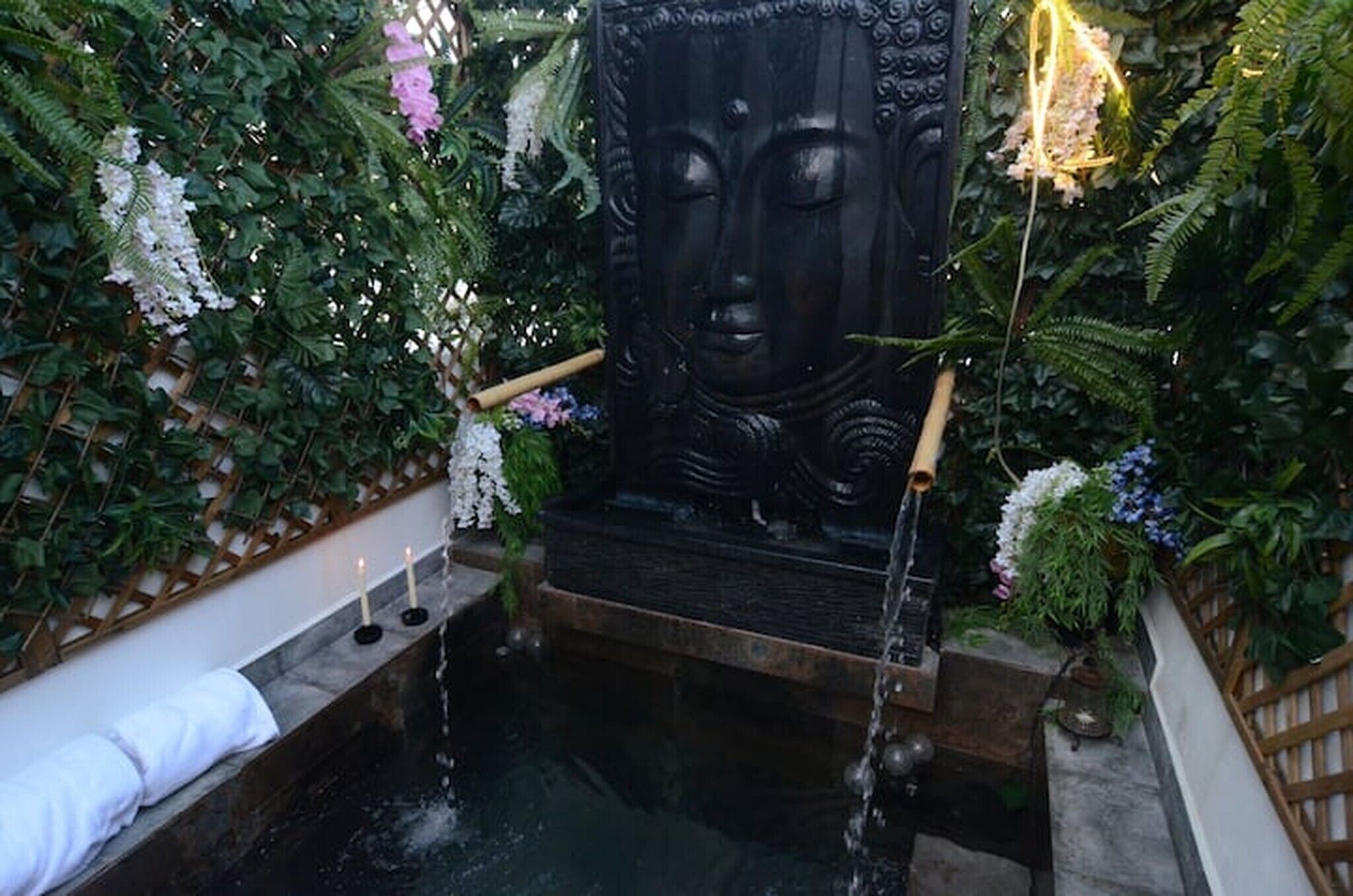 Een rustige tuin met een Boeddhabeeld, een vijver en weelderige begroeiing.