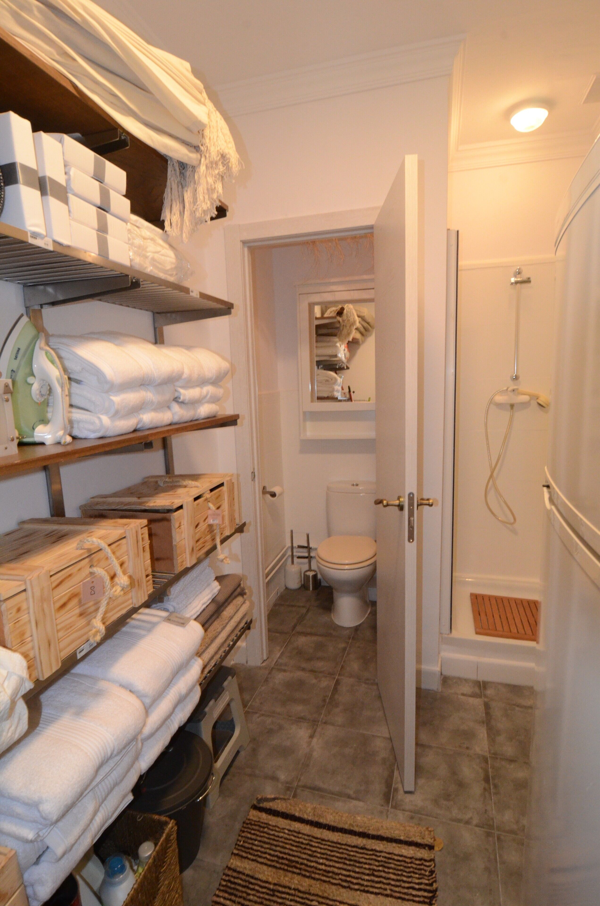 A bathroom with a shower, toilet, and shelves with towels.