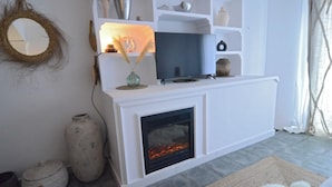 Una sala de estar con chimenea, televisor y objetos decorativos en estantes.