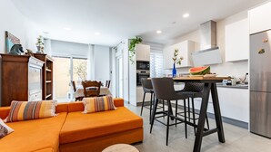 A modern living room with a sofa, a dining area with chairs, a kitchen with a refrigerator, and a window. - Apartment 'Apartamento Novasol' with Private Terrace, Wi-Fi and Air Conditioning (Fuengirola)