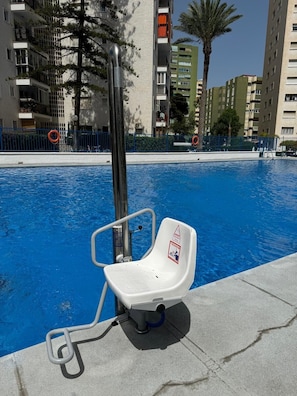 A swimming pool with a lifeguard chair, a metal pole, and a blue fence. - Apartment 'Nuevo Acapulco' with Mountain View, Shared Pool and Shared Garden (Fuengirola)