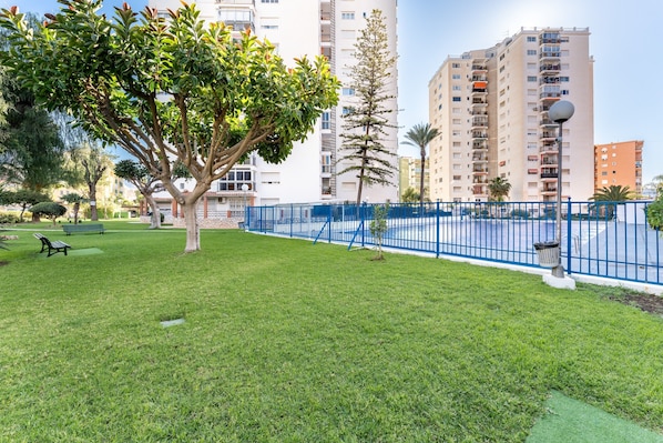 A grassy area with a tree, a bench, and a blue fence. - Apartment 'Nuevo Acapulco' with Mountain View, Shared Pool and Shared Garden (Fuengirola)