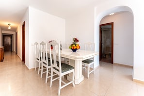 A dining area with a white table and chairs, a fruit bowl on the table, and a tiled floor. - Apartment 'Nuevo Acapulco' with Mountain View, Shared Pool and Shared Garden (Fuengirola)