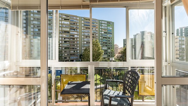 Ein Balkon mit Tisch und Stühlen, großen Fenstern und Blick auf hohe Gebäude.