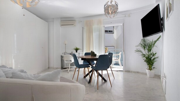 Un salon moderne comprenant un canapé, une table à manger, des chaises, un téléviseur fixé au mur et une plante en pot.