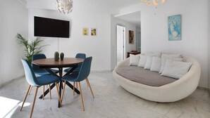 Un salon moderne avec une table à manger ronde, des chaises bleues, un canapé beige, un téléviseur à écran plat et un luminaire au plafond original.