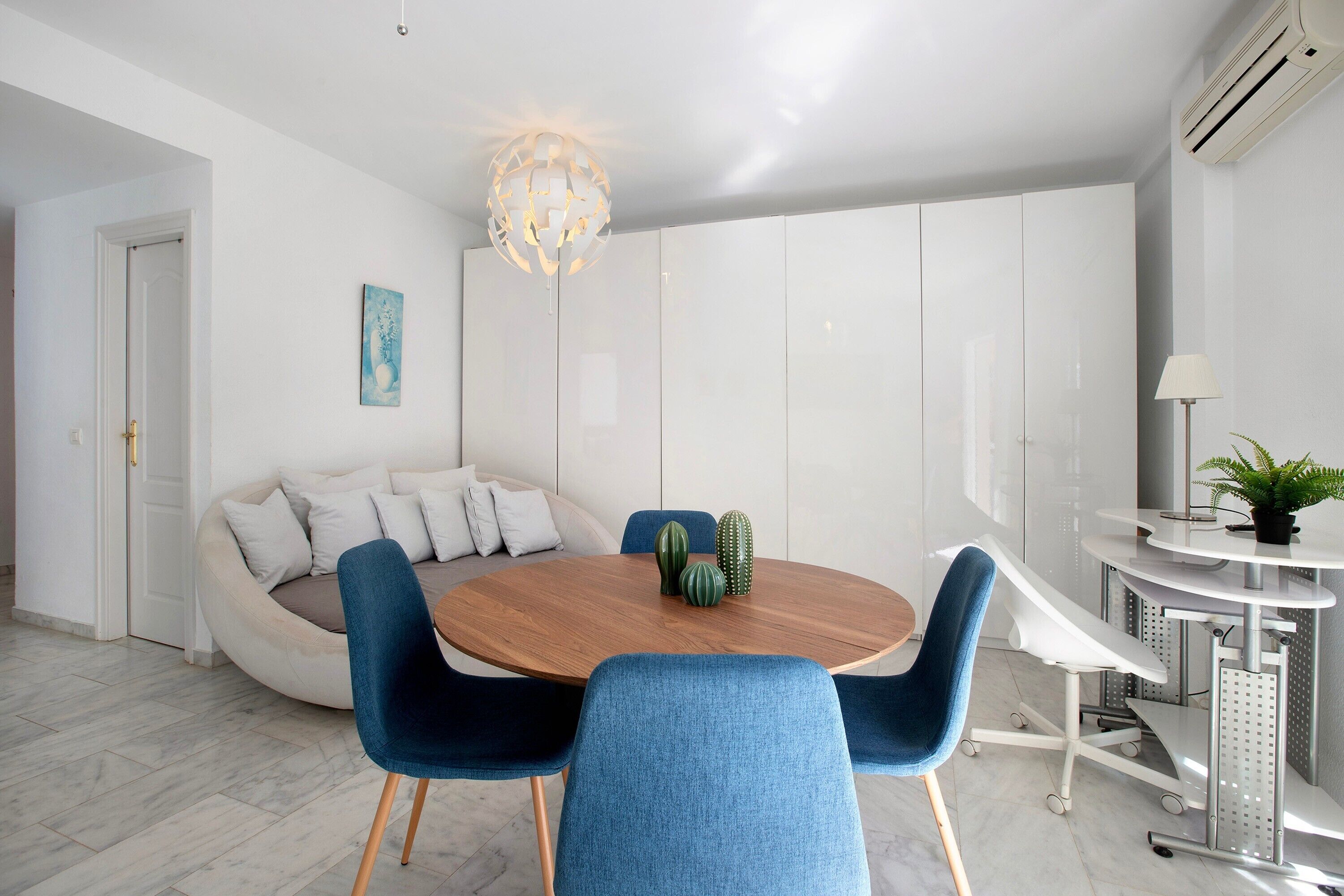 Un comedor moderno con una mesa redonda de madera, sillas tapizadas en azul, una lámpara esférica original y un armario blanco al fondo.