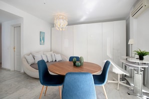 Ein moderner Essbereich mit einem runden Holztisch, blau gepolsterten Stühlen, einer ungewöhnlichen, kugelförmigen Leuchte und einem weißen Schrank im Hintergrund.