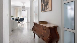 Un couloir avec une commode en bois, un coin repas avec des chaises et une table, et un tableau représentant des éléphants accroché au mur.